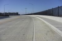 an empty freeway with two lanes with lights over the street and buildings behind it and two lanes on each side,