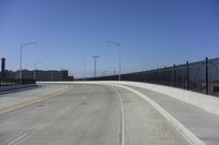 an empty freeway with two lanes with lights over the street and buildings behind it and two lanes on each side,