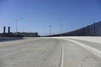 an empty freeway with two lanes with lights over the street and buildings behind it and two lanes on each side,