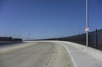 an empty freeway with two lanes with lights over the street and buildings behind it and two lanes on each side,