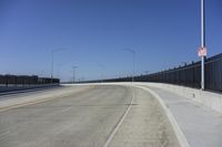 an empty freeway with two lanes with lights over the street and buildings behind it and two lanes on each side,