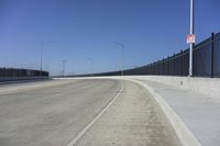 an empty freeway with two lanes with lights over the street and buildings behind it and two lanes on each side,