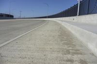 an empty freeway with two lanes with lights over the street and buildings behind it and two lanes on each side,