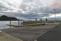 a paved path near a pier with a large body of water on one side and a mountain in the distance