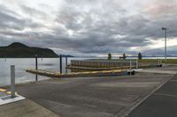 a paved path near a pier with a large body of water on one side and a mountain in the distance