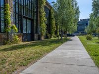 a sidewalk next to the brick building near trees in the park with lots of windows