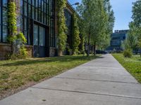 a sidewalk next to the brick building near trees in the park with lots of windows