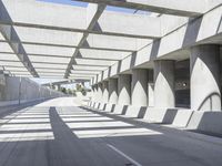 sun shines through the long shadows of concrete structures across an empty highway, underpass