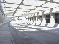 sun shines through the long shadows of concrete structures across an empty highway, underpass