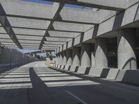 sun shines through the long shadows of concrete structures across an empty highway, underpass