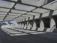 sun shines through the long shadows of concrete structures across an empty highway, underpass