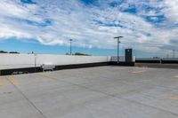 the empty parking lot has a white fence and sky with clouds in the background that are blue and white