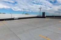 the empty parking lot has a white fence and sky with clouds in the background that are blue and white