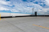 the empty parking lot has a white fence and sky with clouds in the background that are blue and white