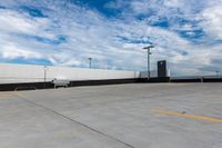 the empty parking lot has a white fence and sky with clouds in the background that are blue and white