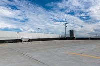 the empty parking lot has a white fence and sky with clouds in the background that are blue and white