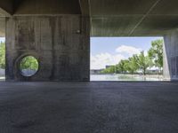 a concrete tunnel in the middle of a park with water running down it and trees around