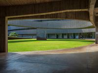 the concrete walkway in front of a circular building with multiple pillars, leading to a grassy area and lawn