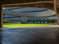 the concrete walkway in front of a circular building with multiple pillars, leading to a grassy area and lawn