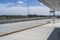 the walkway is concrete at the train station and beside the street is an empty parking space