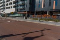 the empty street of the modern urban business district by an apartment complex and sidewalk with multiple red, orange - brick tiles