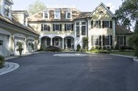 a driveway is lined with a driveway leading to an enormous house with black shuttered windows