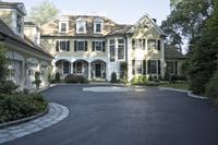 a driveway is lined with a driveway leading to an enormous house with black shuttered windows