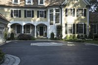 a driveway is lined with a driveway leading to an enormous house with black shuttered windows