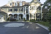 a driveway is lined with a driveway leading to an enormous house with black shuttered windows