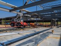 a red vehicle driving in an open floor building under construction, with a worker on a fork lifting a large beam to put metal in place