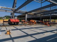 a crane stands in an industrial looking structure with several construction tools and equipment behind it