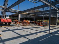 a crane stands in an industrial looking structure with several construction tools and equipment behind it