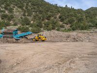 two yellow bulldozers work on sand and gravel in a mountain valley while another one looks at it