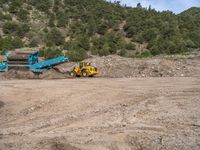 two yellow bulldozers work on sand and gravel in a mountain valley while another one looks at it