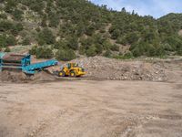 two yellow bulldozers work on sand and gravel in a mountain valley while another one looks at it