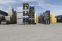 large stacks of yellow, green and black containers next to two rows of blue and white pallets