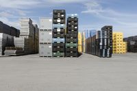 large stacks of yellow, green and black containers next to two rows of blue and white pallets