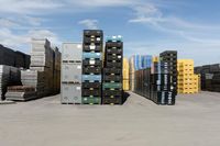 large stacks of yellow, green and black containers next to two rows of blue and white pallets