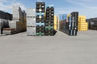 large stacks of yellow, green and black containers next to two rows of blue and white pallets