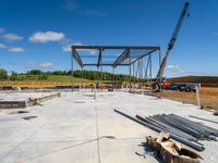 a construction site with a large metal structure and a crane in the background on a sunny day