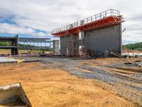 a large concrete structure sitting in the dirt next to a building under construction in a field