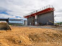 a large concrete structure sitting in the dirt next to a building under construction in a field