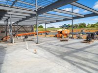 the large concrete building has a steel roof and lots of machinery in the area under the large canopy