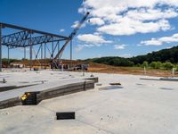 a metal structure sits in a construction site under a blue sky filled with clouds and a person working with machinery