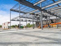 a steel structure under construction with metal beams and orange tubes on the ground in an open space