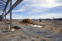 a construction site under a blue sky with some cars under it and a large yellow bulldozer