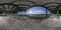 a panoramagraph photograph taken from below an oval roof in a construction site with the sun setting