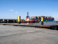 a large blue barge is next to the dock in the harbor, with people standing on the docks edge