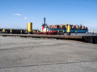 a large blue barge is next to the dock in the harbor, with people standing on the docks edge