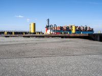 a large blue barge is next to the dock in the harbor, with people standing on the docks edge